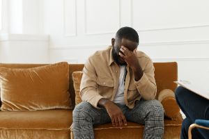 Person Sitting On Couch, Holding Hand To Forehead, Dealing With Symptoms Of Anxiety.