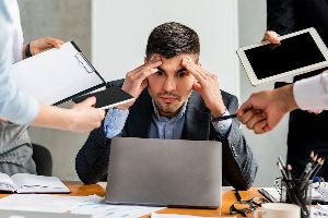 Person At Work In Front Of A Laptop While Fielding Requests From A Variety Of Coworkers.